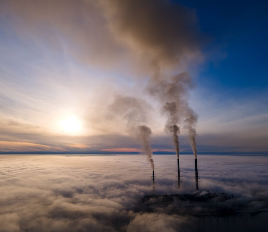 Aerial view of coal power plant high pipes with black smoke moving up polluting atmosphere at sunset.