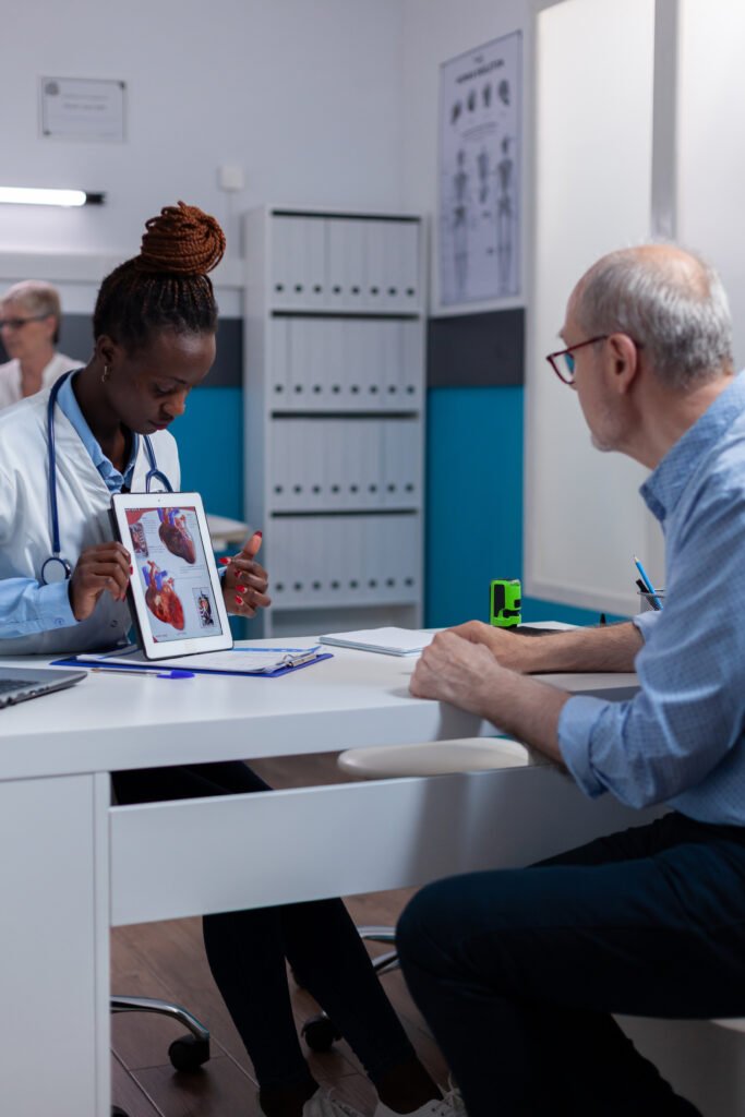 Black woman with doctor profession showing organs illustration on digital tablet display sitting at desk.