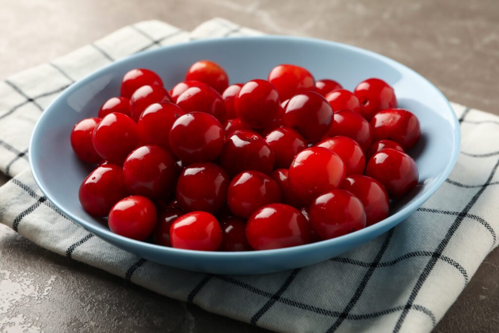 Bowl with red cherry and towel on gray background, close up