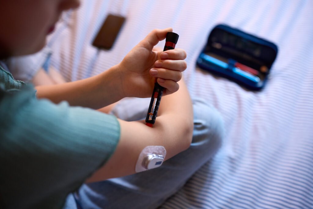 Close Up Of Diabetic Girl On Bed In At Home Using Insulin Pen To Measure To Check Blood Sugar Level