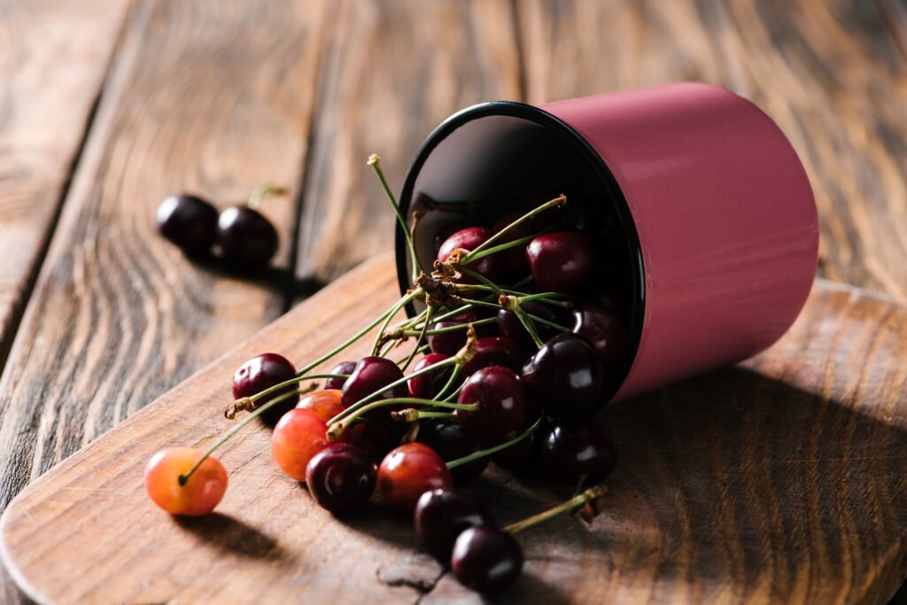 close up view of ripe fresh sweet cherries in pink cup on wooden cutting board on table