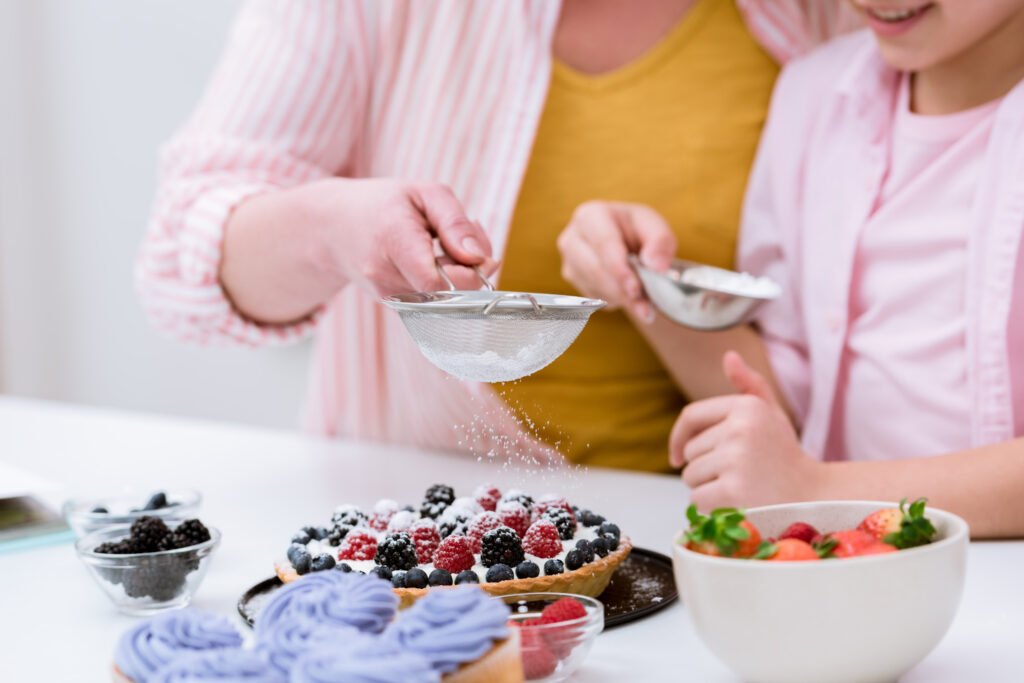 grandmother and little granddaughter pouring sugar powder onto tart with berries to make dessert for diabetics