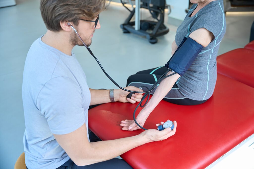 Guy with glasses measures the blood pressure of an elderly woman, people sit in a gym