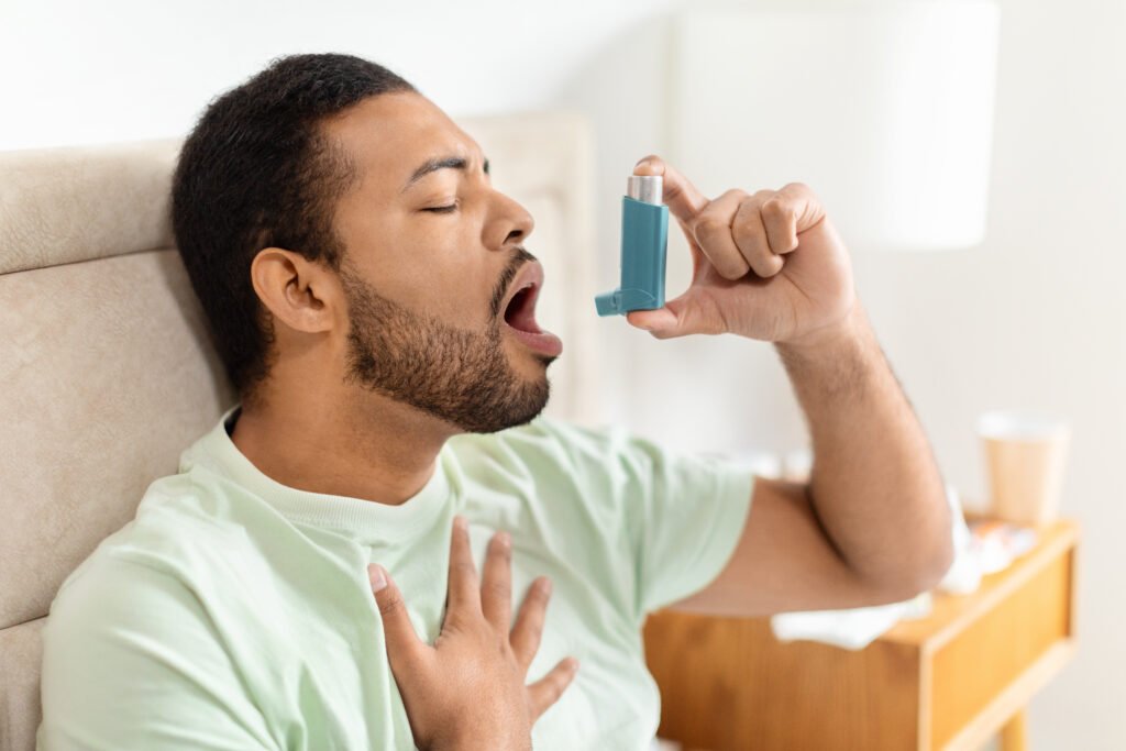 Man sitting alone in bed at home and using an asthma pump.