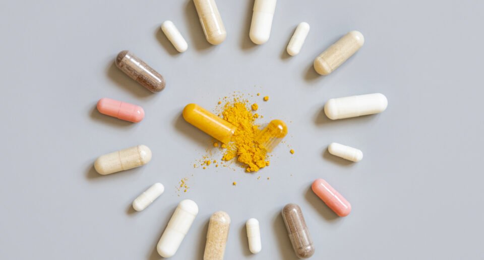 Assorted medical capsules in a circle with one opened to show yellow powder on grey top view. Preventive medicine and healthcare, dietary supplements and vitamins