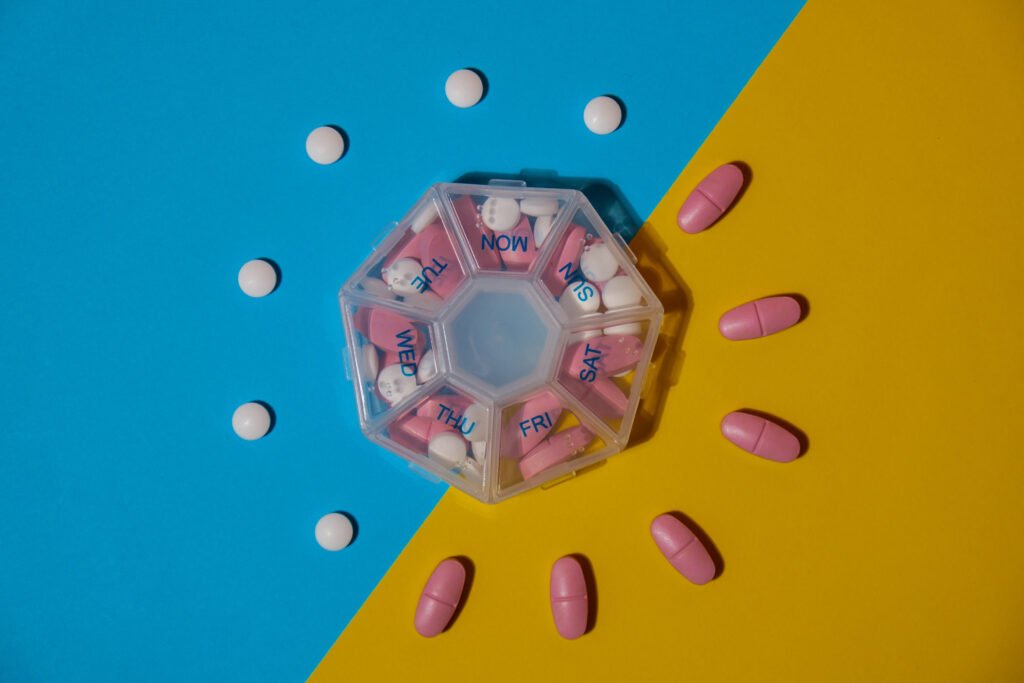 Organizer weekly shots medical pill box with doses of tablets for daily take medicine with white pink drugs and capsules.