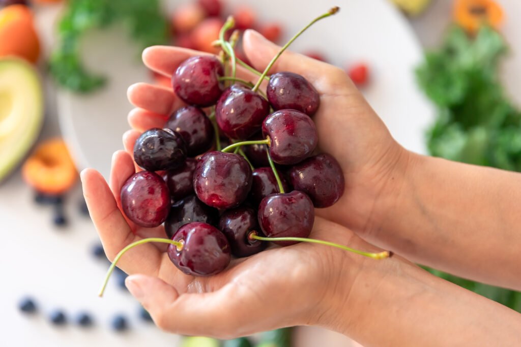 Ripe cherries in female hands on a blurred background of vegetables and fruits, summer food concept.