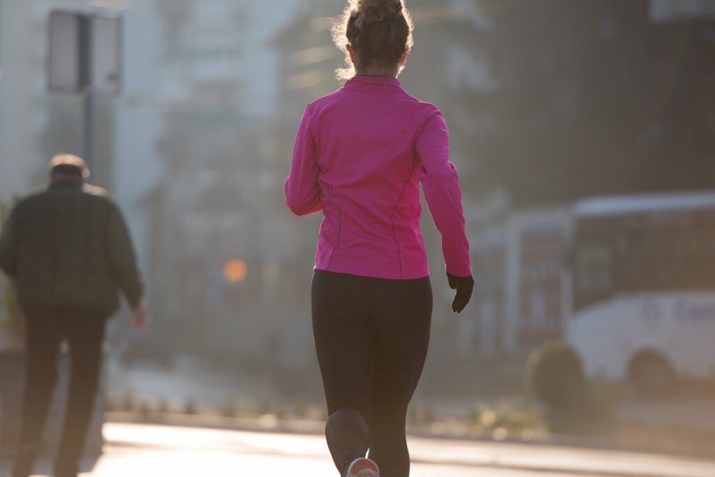 sporty woman running on sidewalk at early morning jogging with city  sunrise scene in background