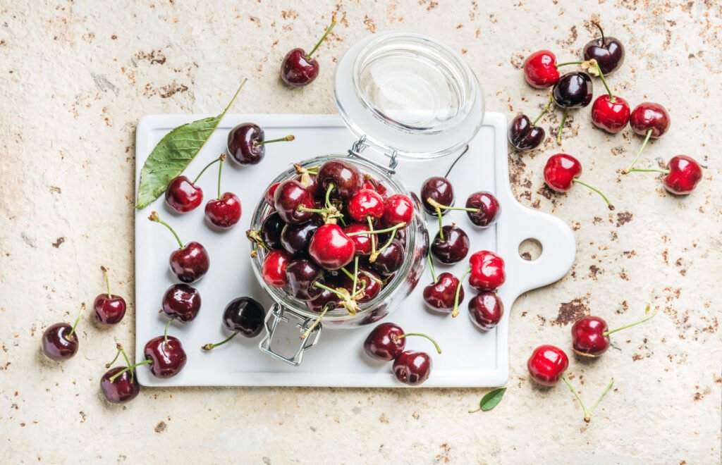 Sweet cherry in glass jar on white ceramic board over concrete background, top view