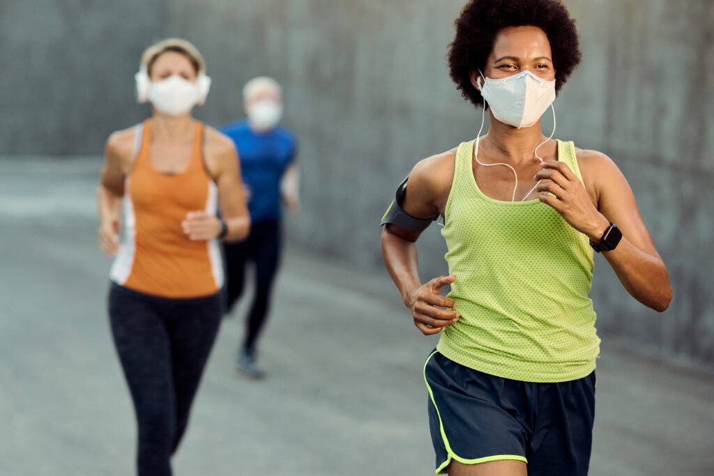 Happy sportswoman wearing protective face mask while running outdoors.