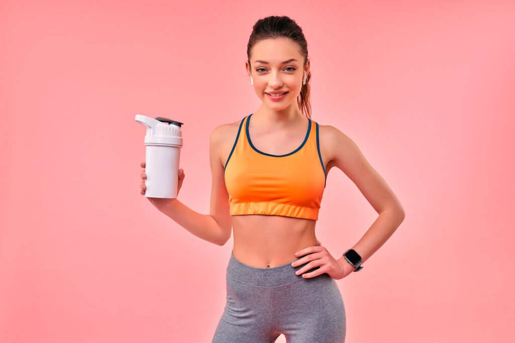 Cute athletic girl in sportswear with protein shake isolated on pink background. Sports, yoga, active lifestyle, exercise for health.