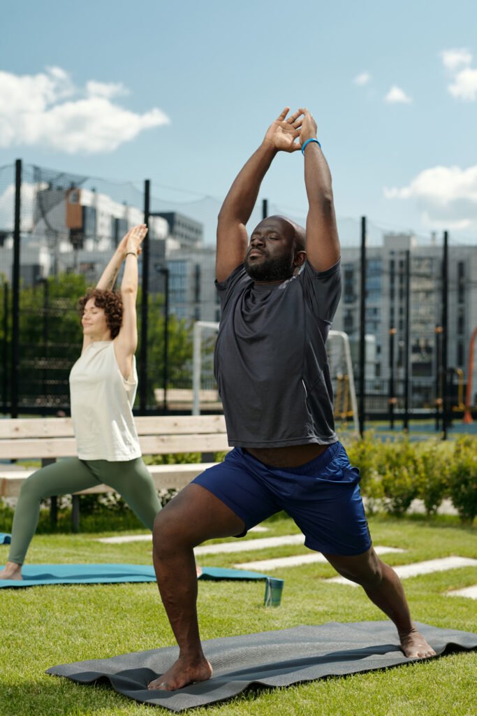 Man in activewear standing on mat on sports ground and exercising while keeping arms raised over head.