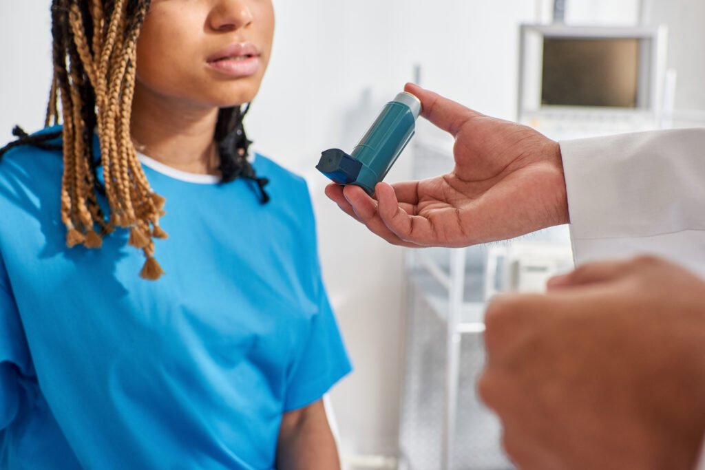 young indian doctor teaching his ill african american female patient how to use inhaler.