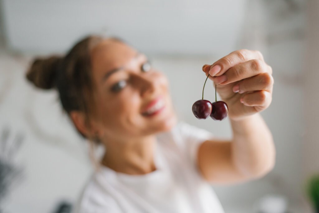 Young woman holds cherries in her hand with a focus on a berry. The concept of healthy nutrition and organic fruit growing.