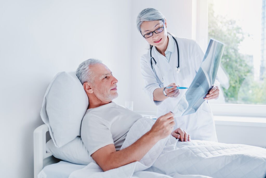 Doctor standing in ward near elderly patient showing picture of an x-ray