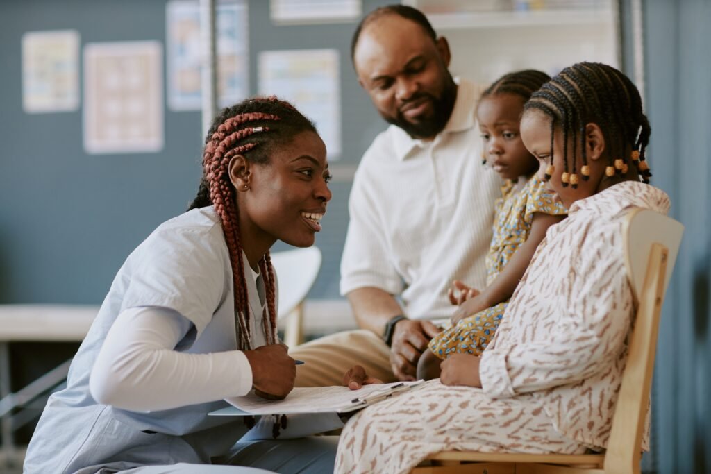 Smiling health care worker engaging with a family in a medical setting, showing compassion and professionalism while two children and a parent observe attentively