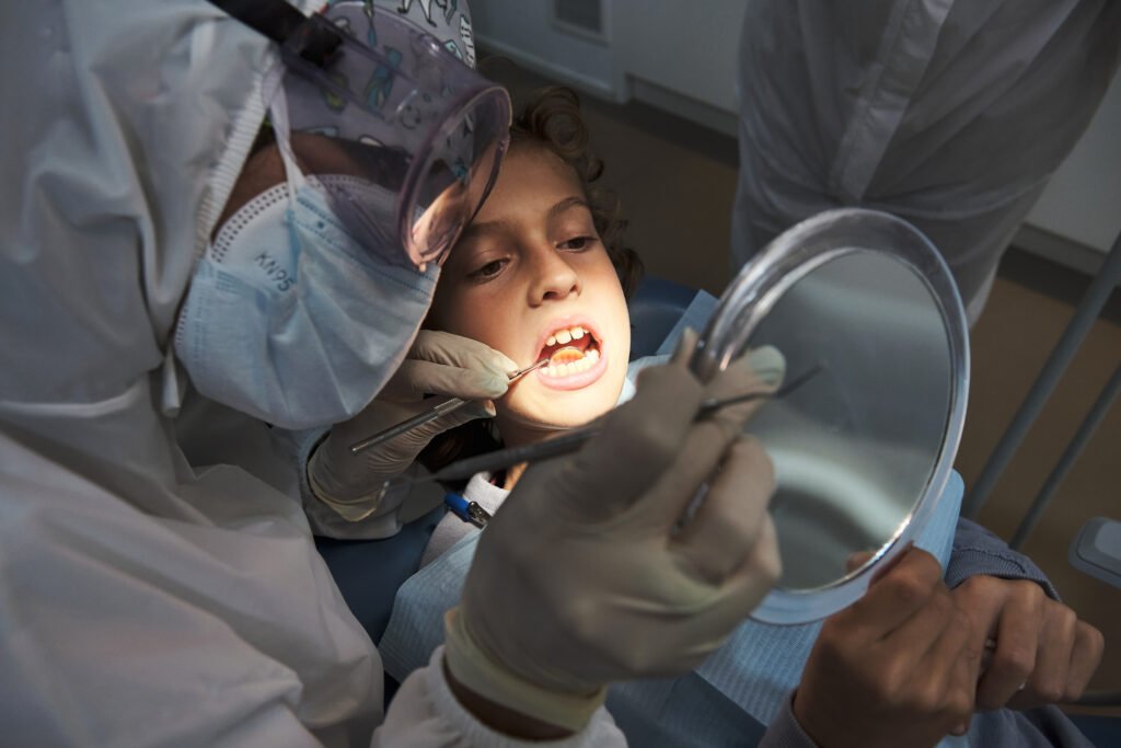 High angle of anonymous dentist in protective costume examining mouth of patient to diagnose the virus coused by surgury drinks with tools in clinic.