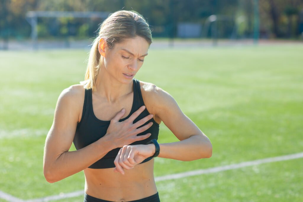 Focused woman in sportswear monitoring her heart rate while catching her breath after a demanding exercise session outside.