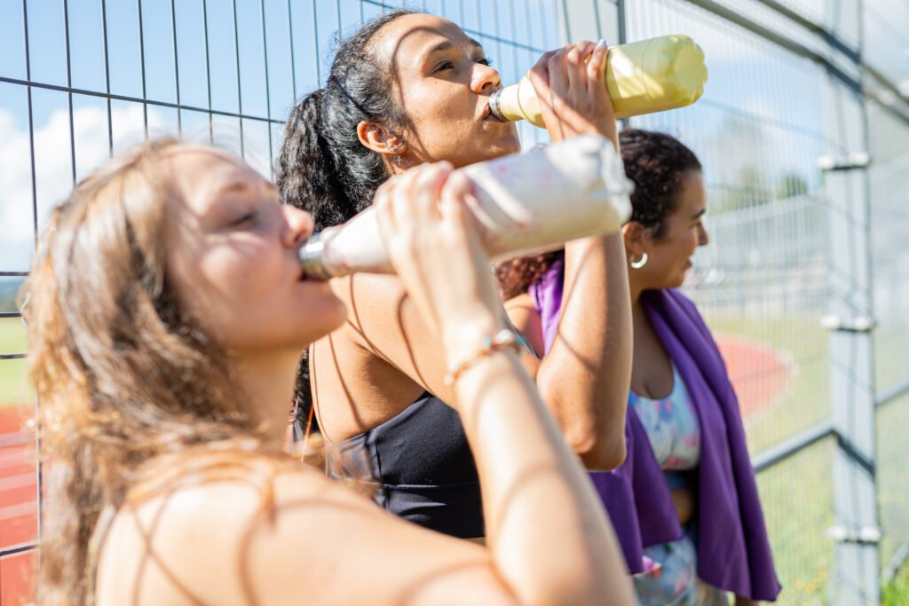 Group of girls drinking water from a thermos after doing exercise. Resting  before do another training series.