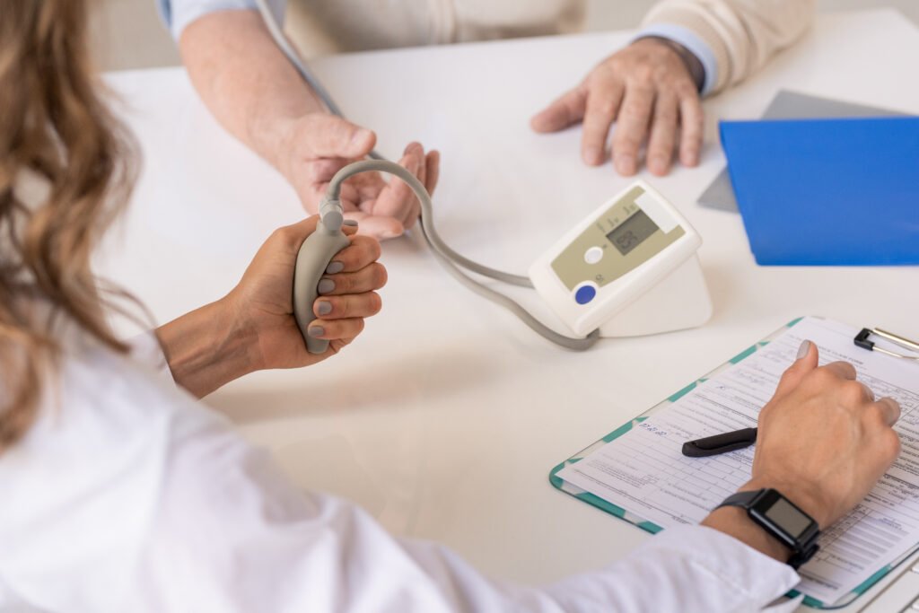 Hands of young therapeutist pressing tonometer pump while measuring blood pressure of senior patient sitting in front of her