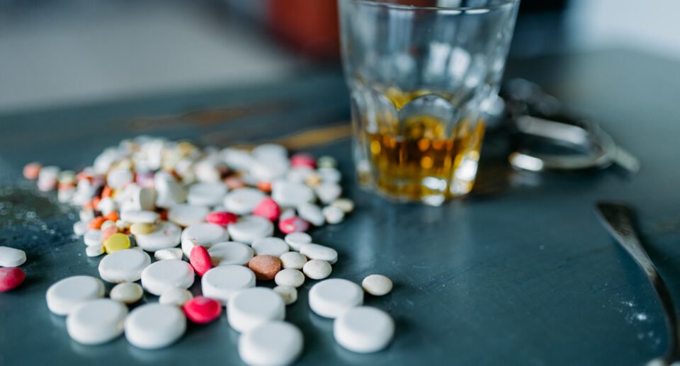 Junkie kit, narcotic concept, addiction problem. Pills are laid out on wooden table, alcohol and handcuff