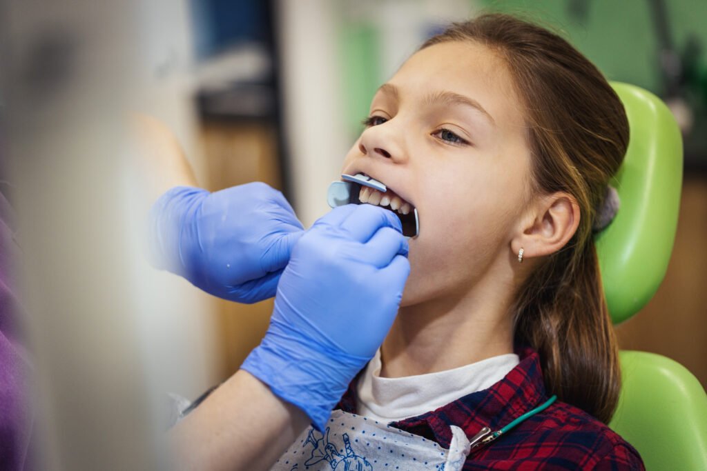 Teenage girl is at the dentist. She sits in the dentist's chair and the dentist sets braces on her teeth.