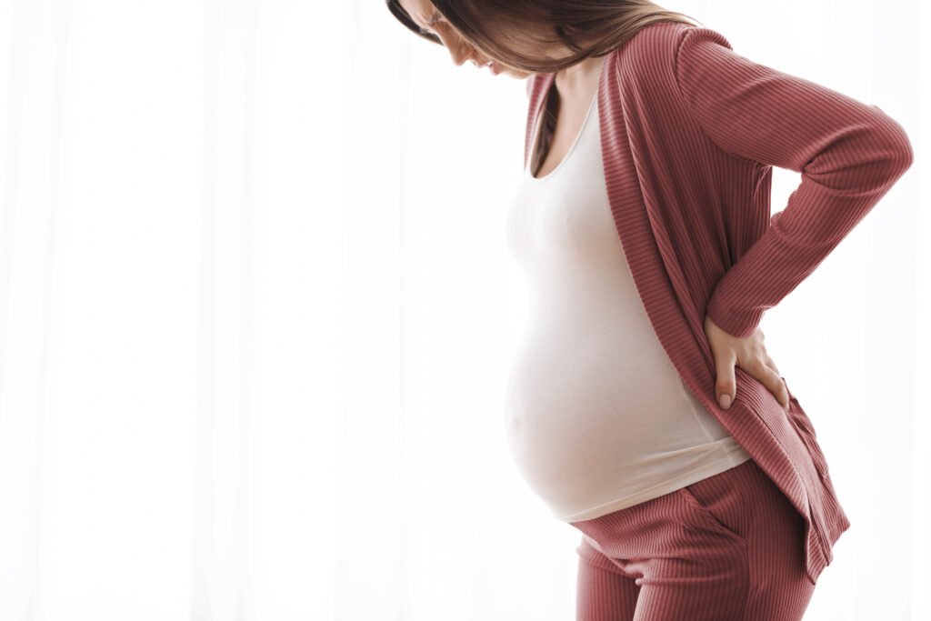 Pregnancy Backache. Closeup Shot Of Young Pregnant Woman Suffering hormonal change Pain, Millennial Expectant Lady Feeling Unwell While Standing Near Window At Home, Side View With Copy Space