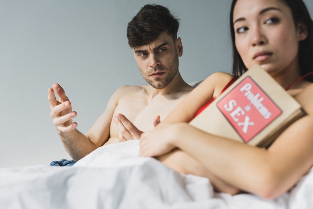 selective focus of offended asian woman holding problems in sex due to hormonal imbalance book while lying near dissatisfied