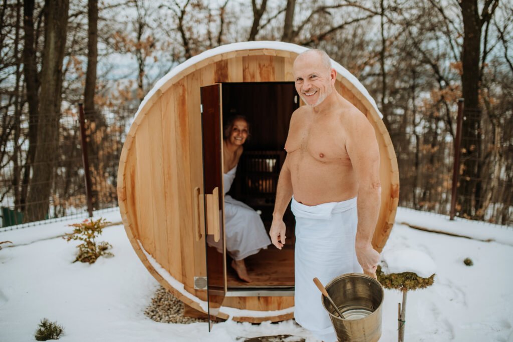 Senior woman in towel with her husband coming out from outdoor sauna during a cold winter day.