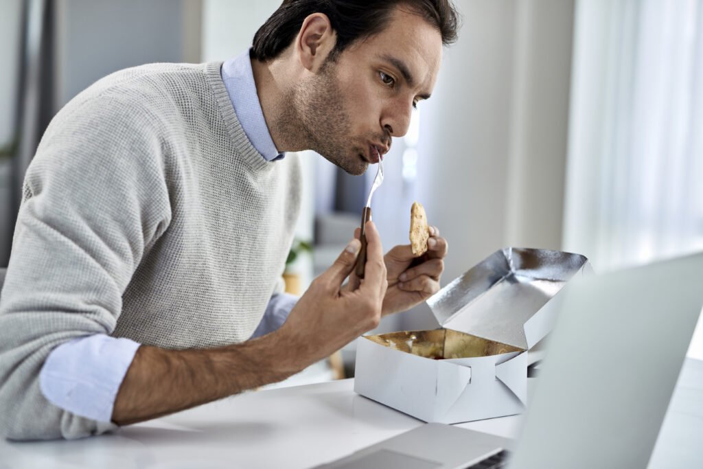 Male entrepreneur having a lunch while working on a computer at home.