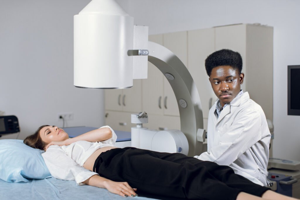 Young high-skilled focused black man doctor in white coat, providing lithotripsy procedure for his lying female patient with modern ultrasonic lithotriptor to break up stones.