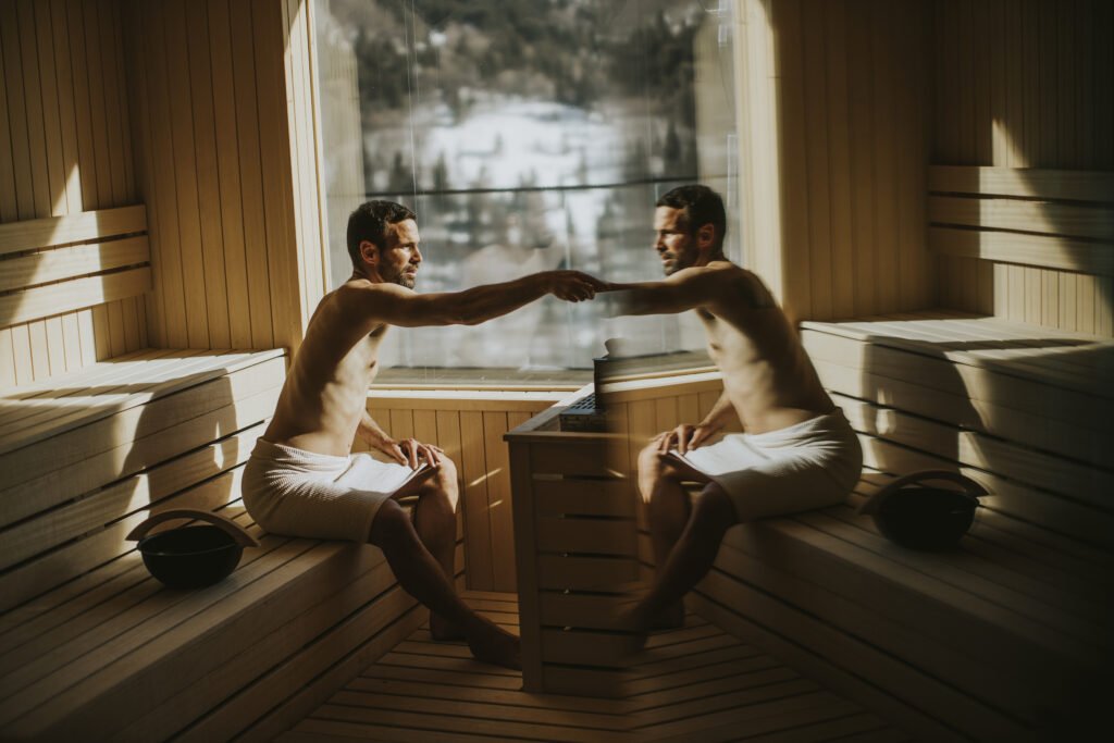 Handsome young man pouring water onto hot stone in the sauna