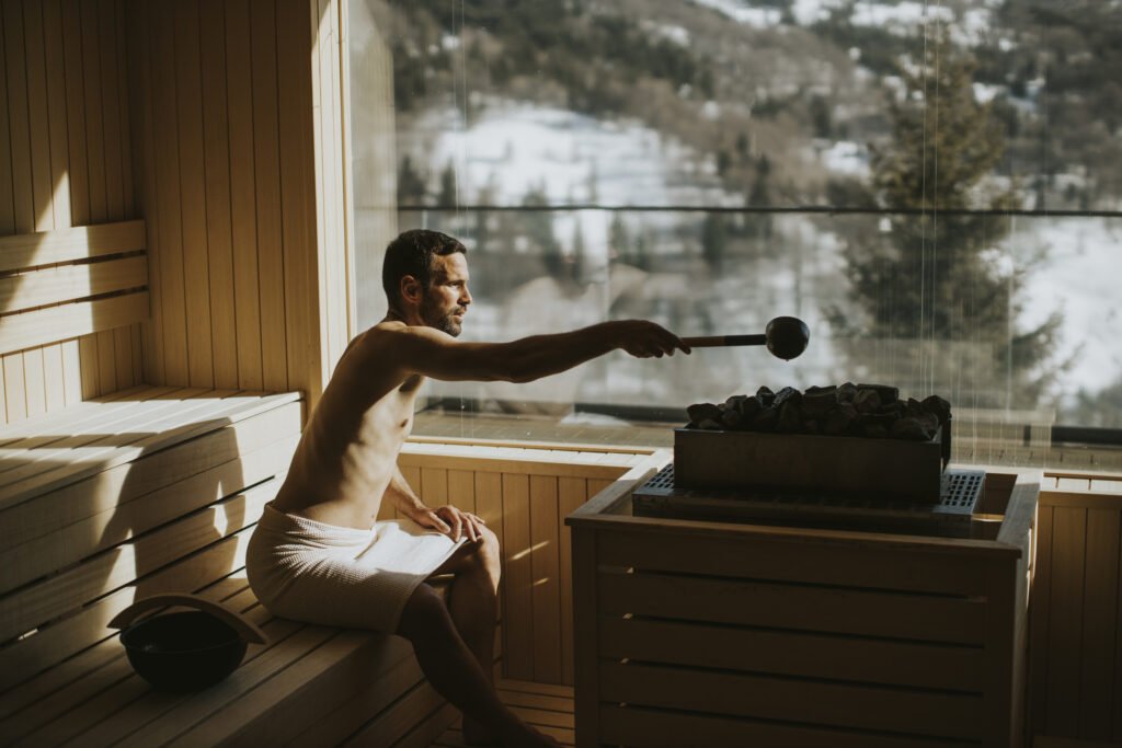 Handsome young man pouring water onto hot stone in the sauna