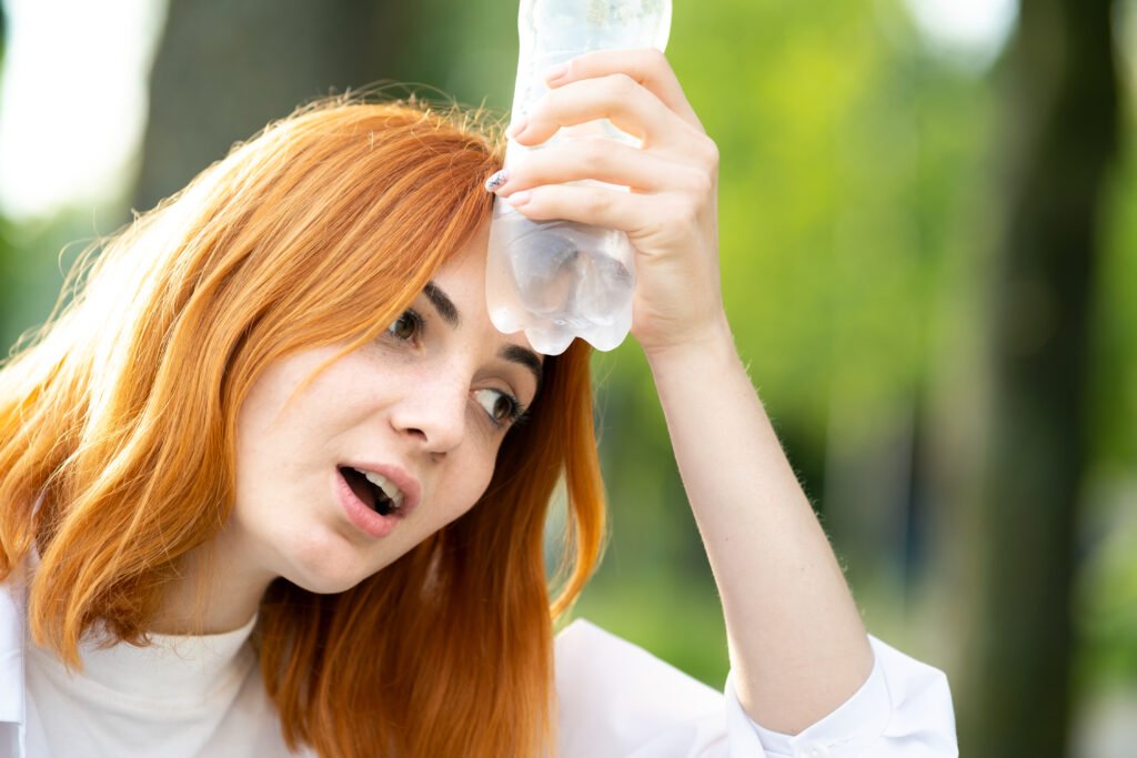 Young tired redhead woman drinking water from a bottle in summer park to make itself safe from dehydration.